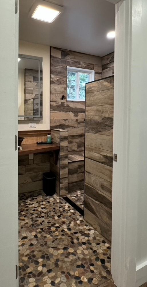 Bathroom with stone tile walls and floor. A walk-in shower is on the right.
