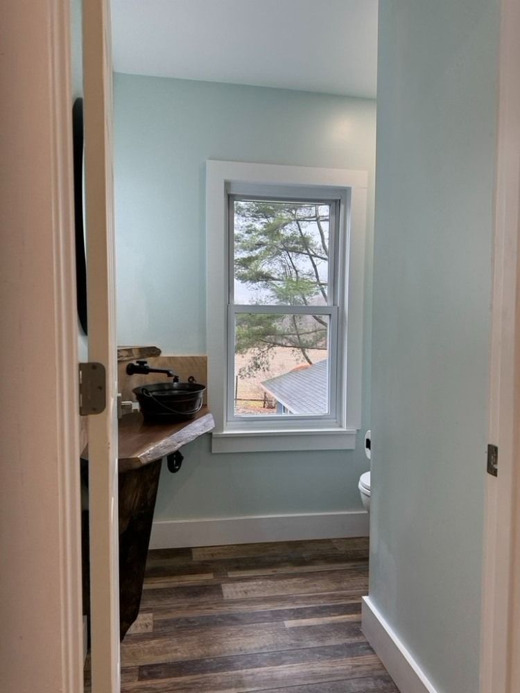 Powder room with light blue walls, a window, and wood-look flooring.