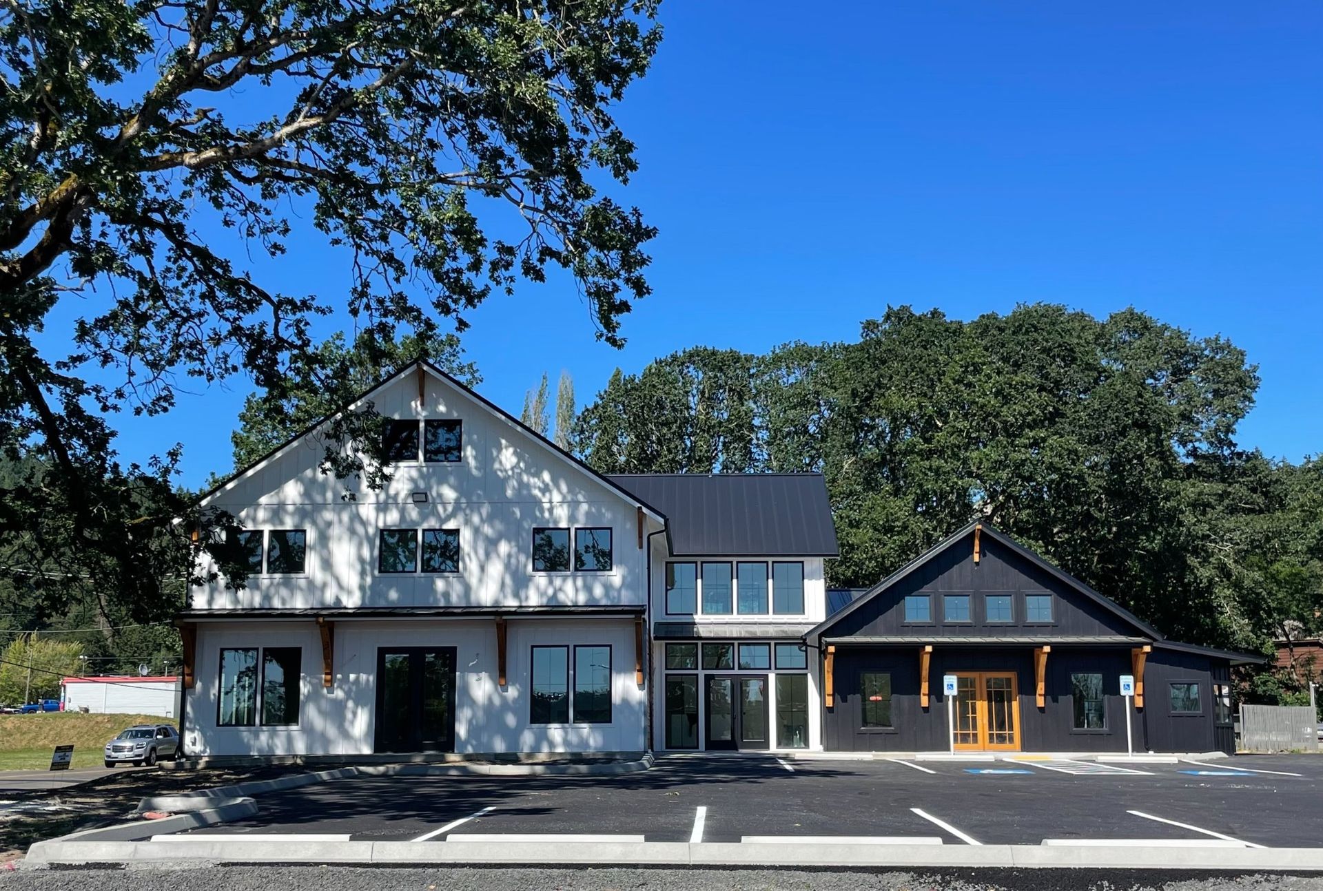 Two-story white and dark gray building with parking lot and trees under a blue sky