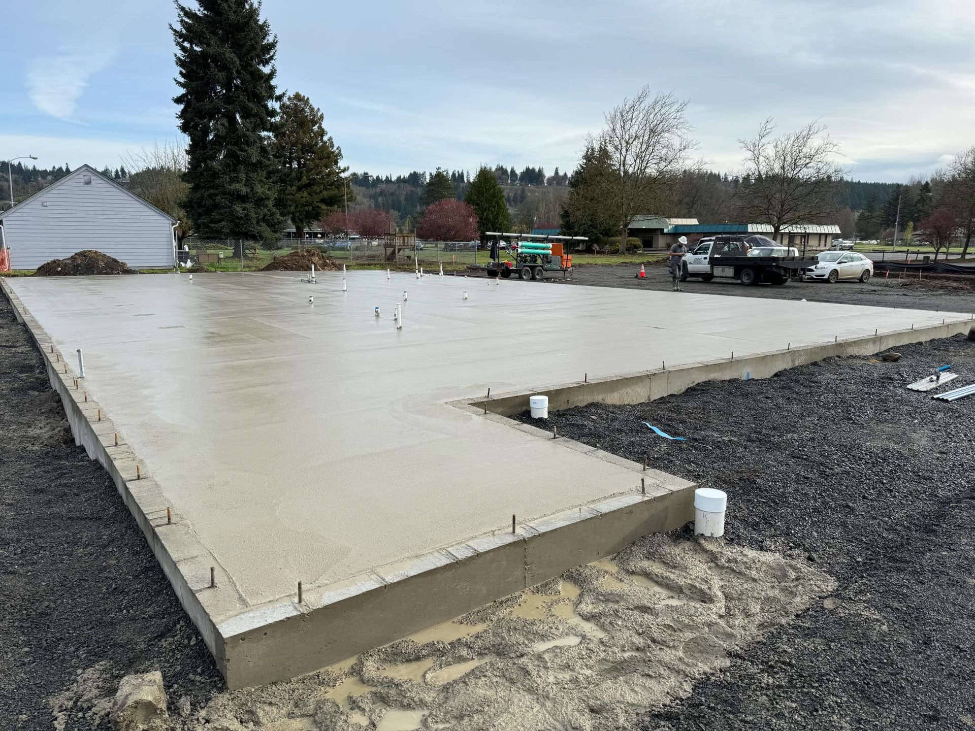 New concrete slab foundation at a construction site with gravel and parked trucks nearby