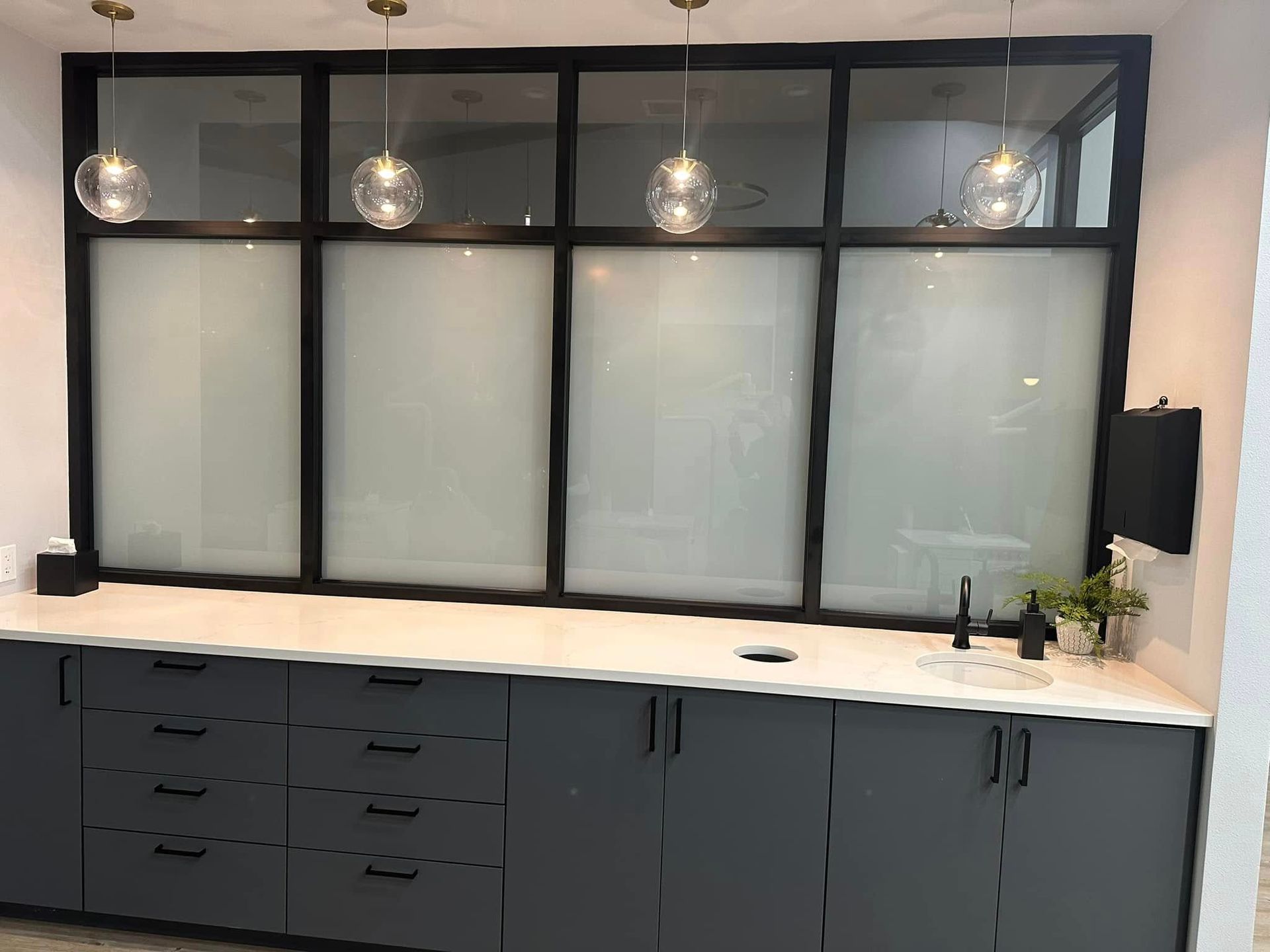 Modern kitchen with dark cabinets, white countertops, frosted glass panels, and pendant lights