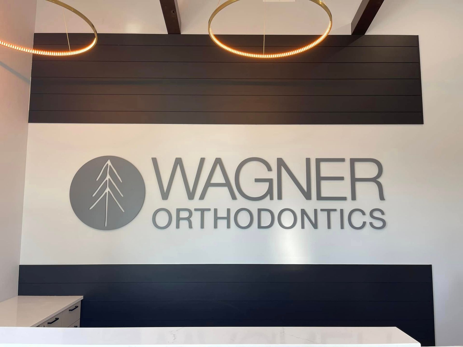 Wagner Orthodontics office wall sign on a white and dark navy interior backdrop with ring lights above