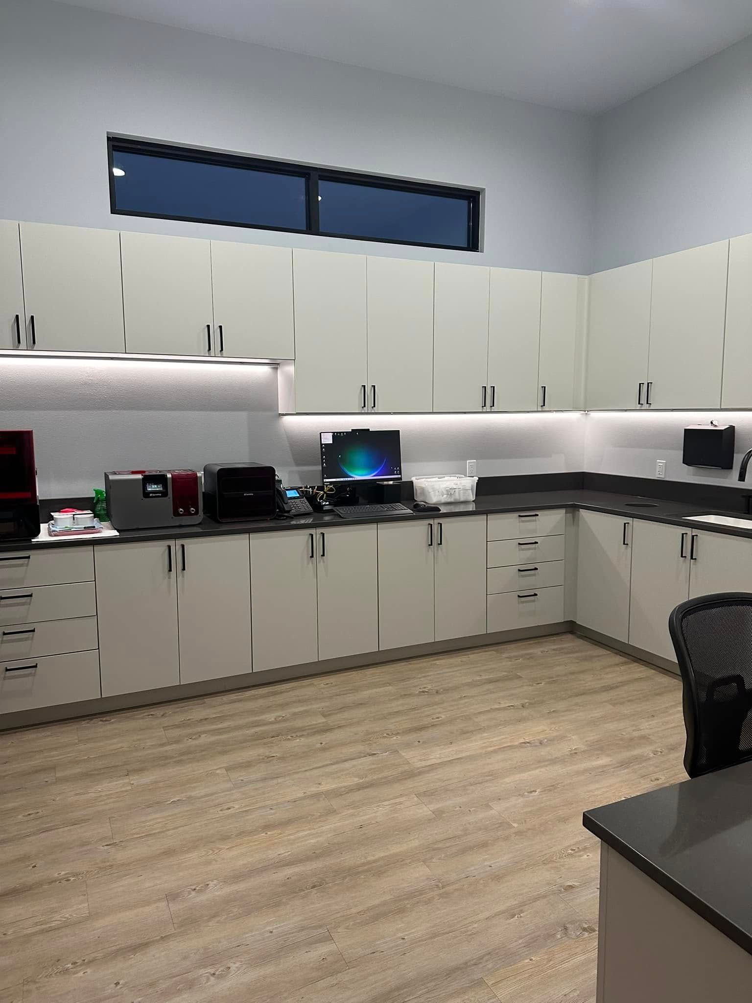 Empty office break room with white cabinets, black countertops, and wood flooring