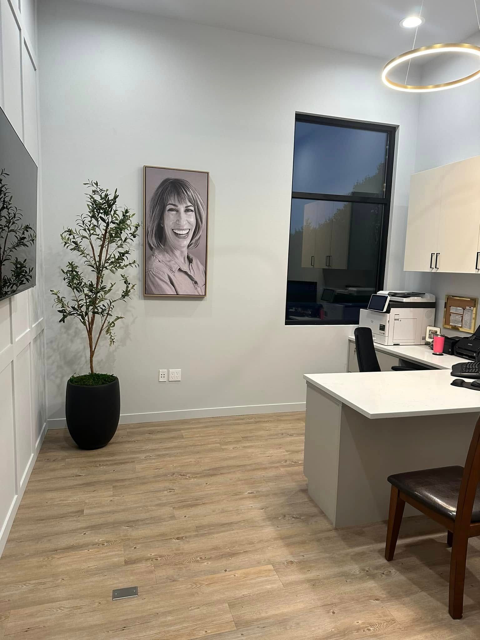 Modern kitchen with wood floor, white cabinets, island, potted plant, portrait art, and window.