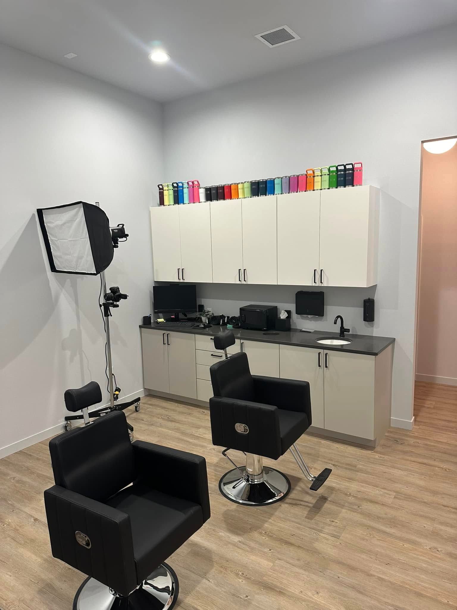 Modern salon workspace with black styling chairs, mirrors, white cabinets, and colorful product display on top