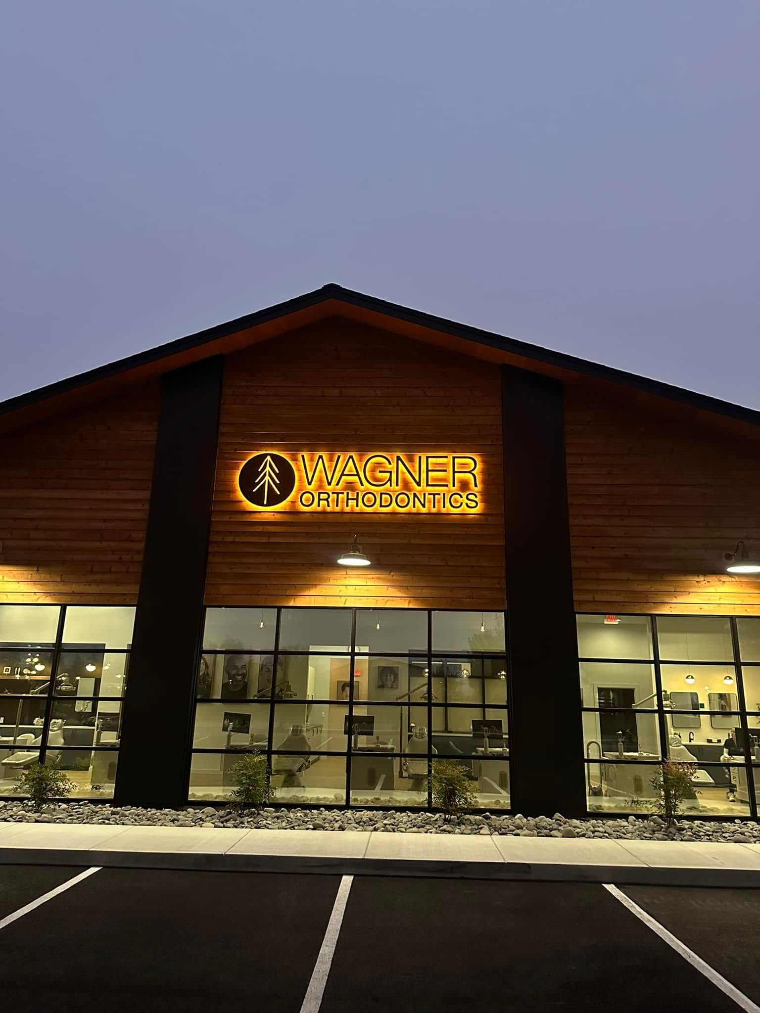 Modern storefront at dusk with illuminated sign, large windows, and empty parking spaces in front