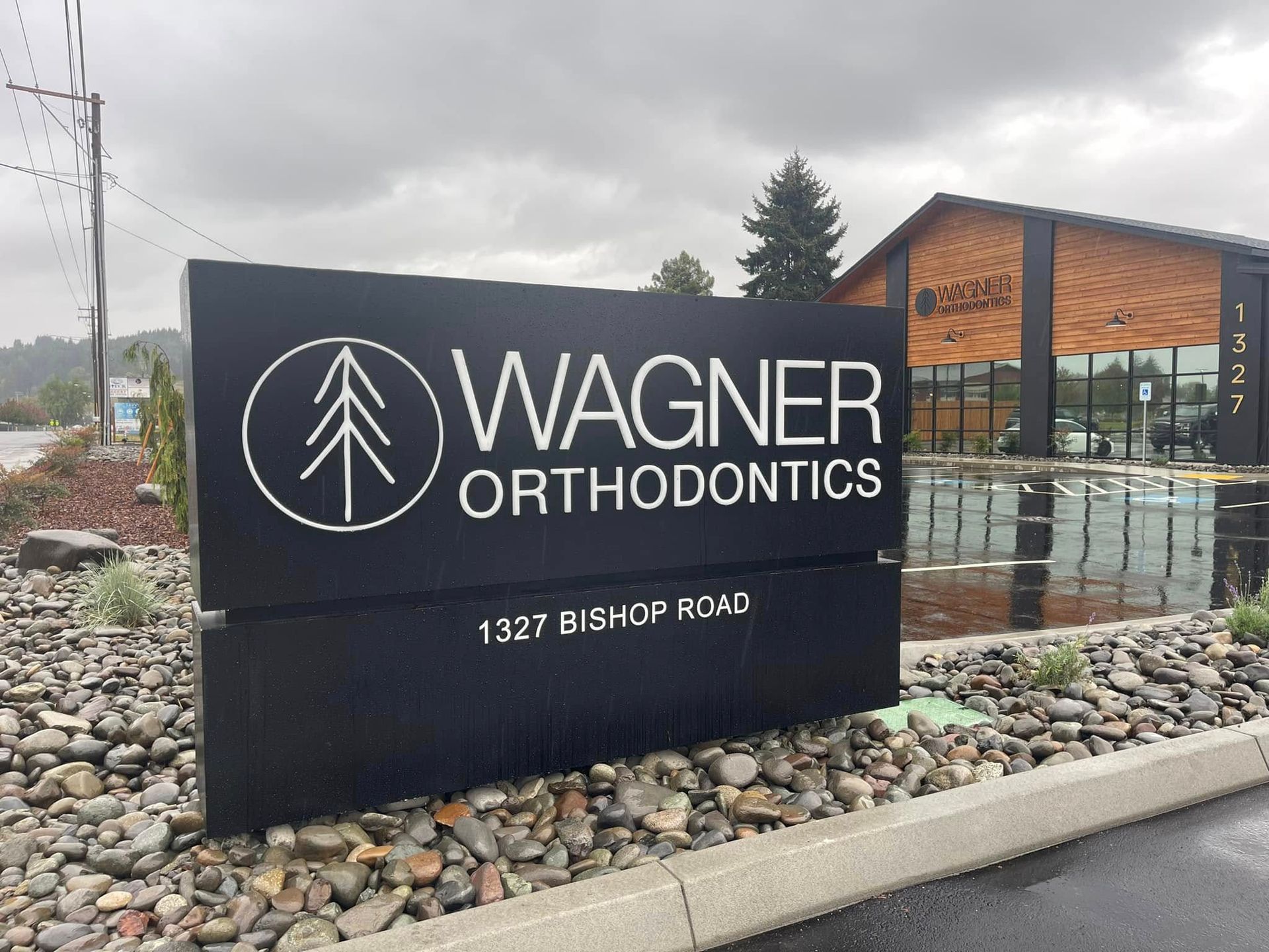 Wagner Orthodontics sign on a black stone monument by the road, with modern building behind it.