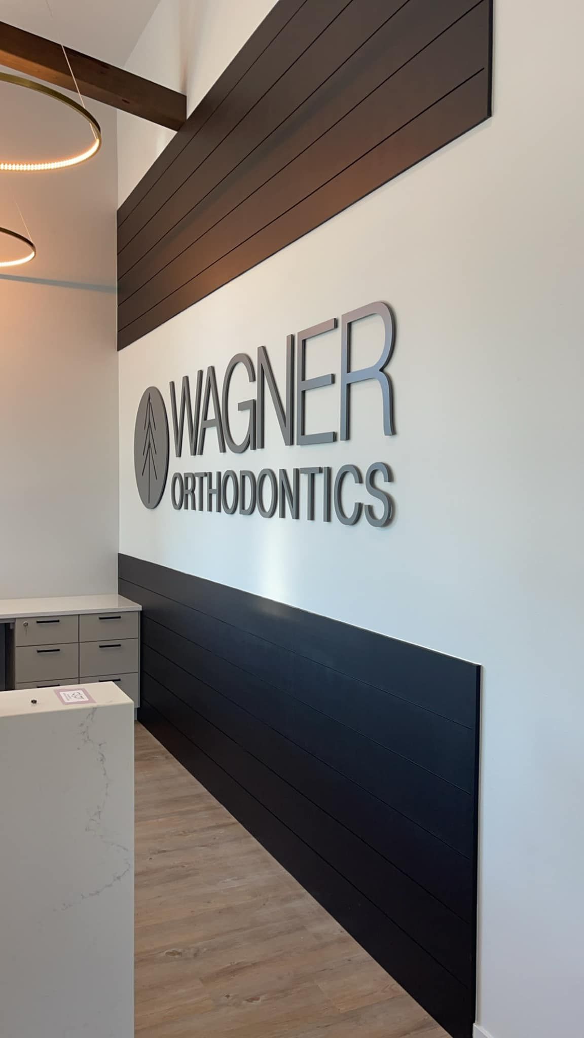 Hallway wall with Mager Orthodontics sign, white walls, dark wood accent, and light wood floor
