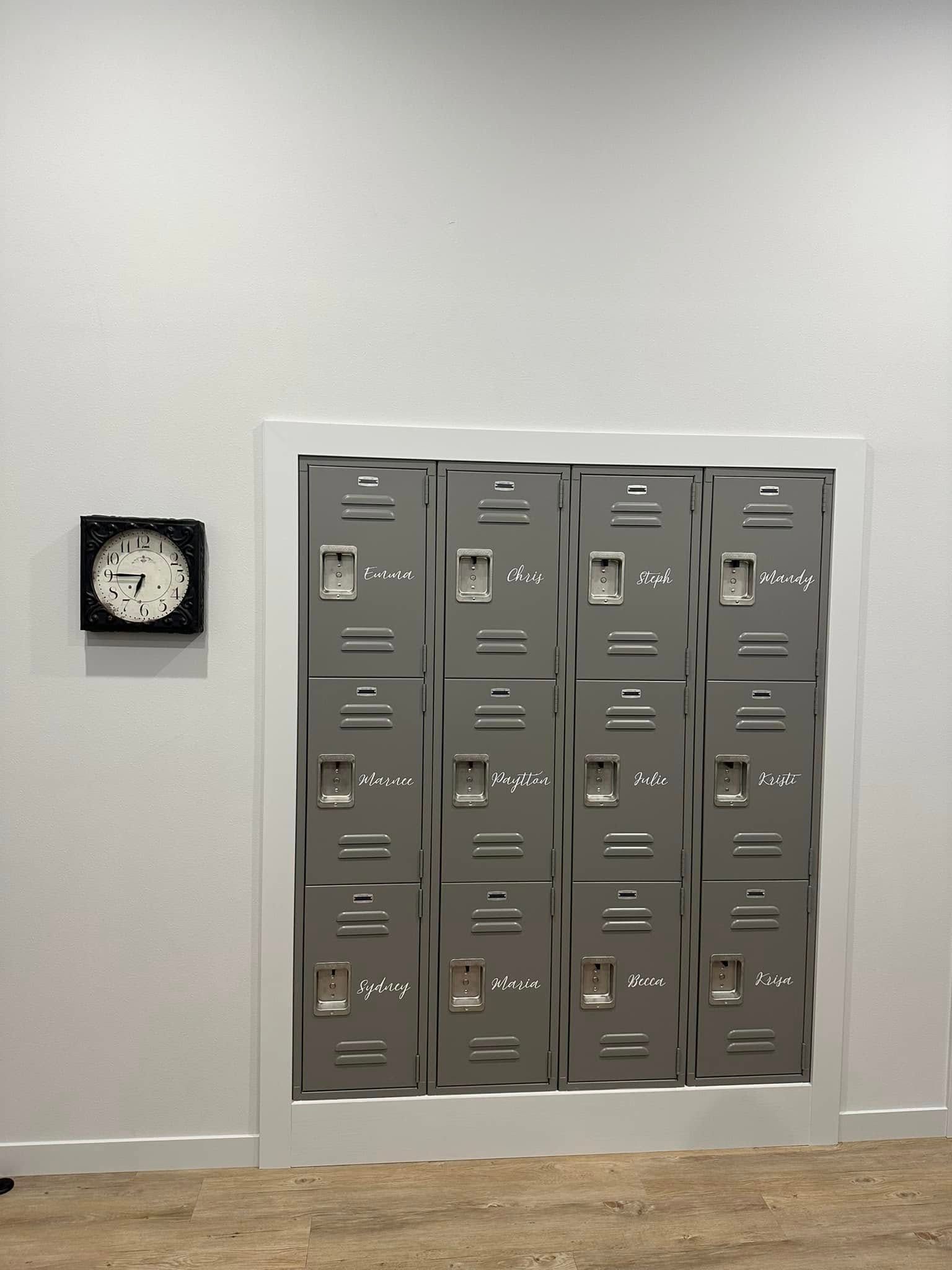 Wall-mounted gray lockers beside a small black-framed clock on a plain white wall.