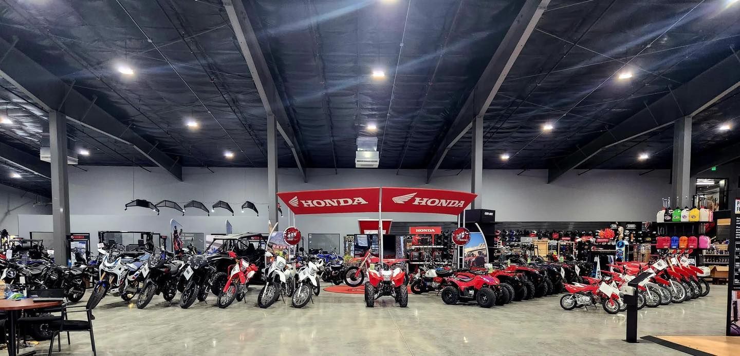 Motorcycle showroom with rows of bikes and red ATVs under bright warehouse lighting