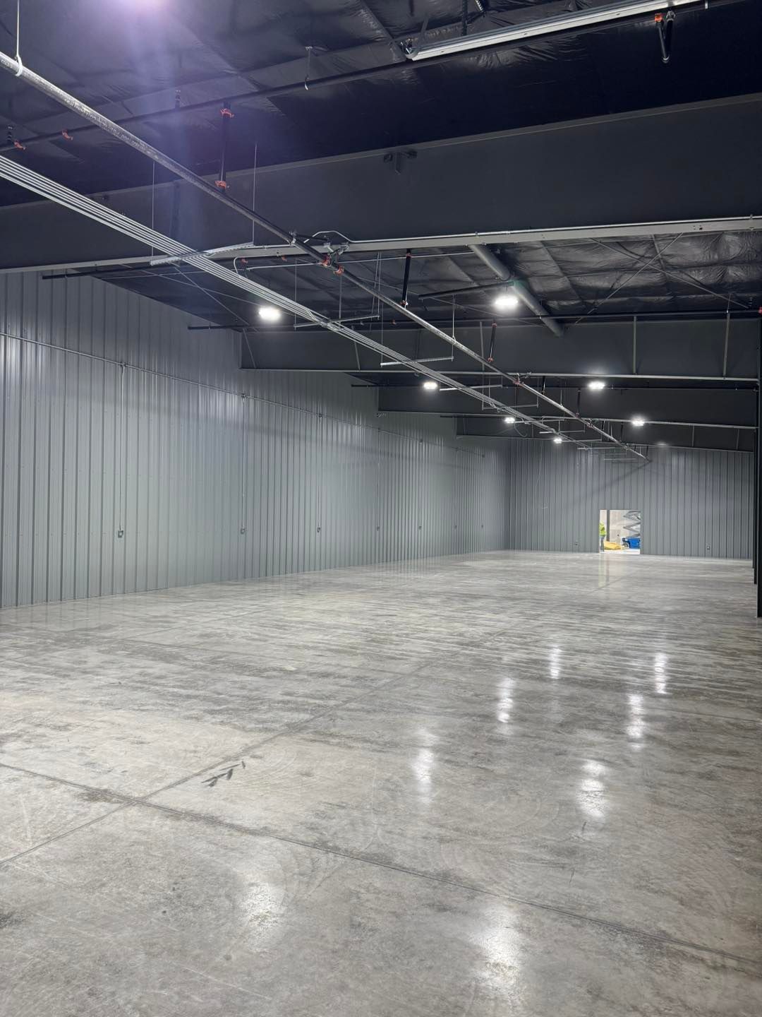 Empty industrial warehouse with polished concrete floor, gray metal walls, and overhead lights