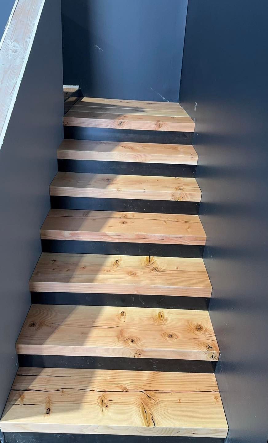 Narrow indoor staircase with unfinished wooden steps and blue-gray walls