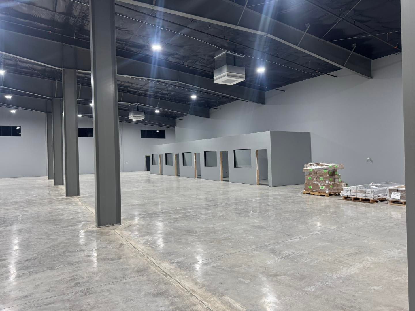 Empty warehouse interior with concrete floor, gray columns, and stacked pallets along the wall.
