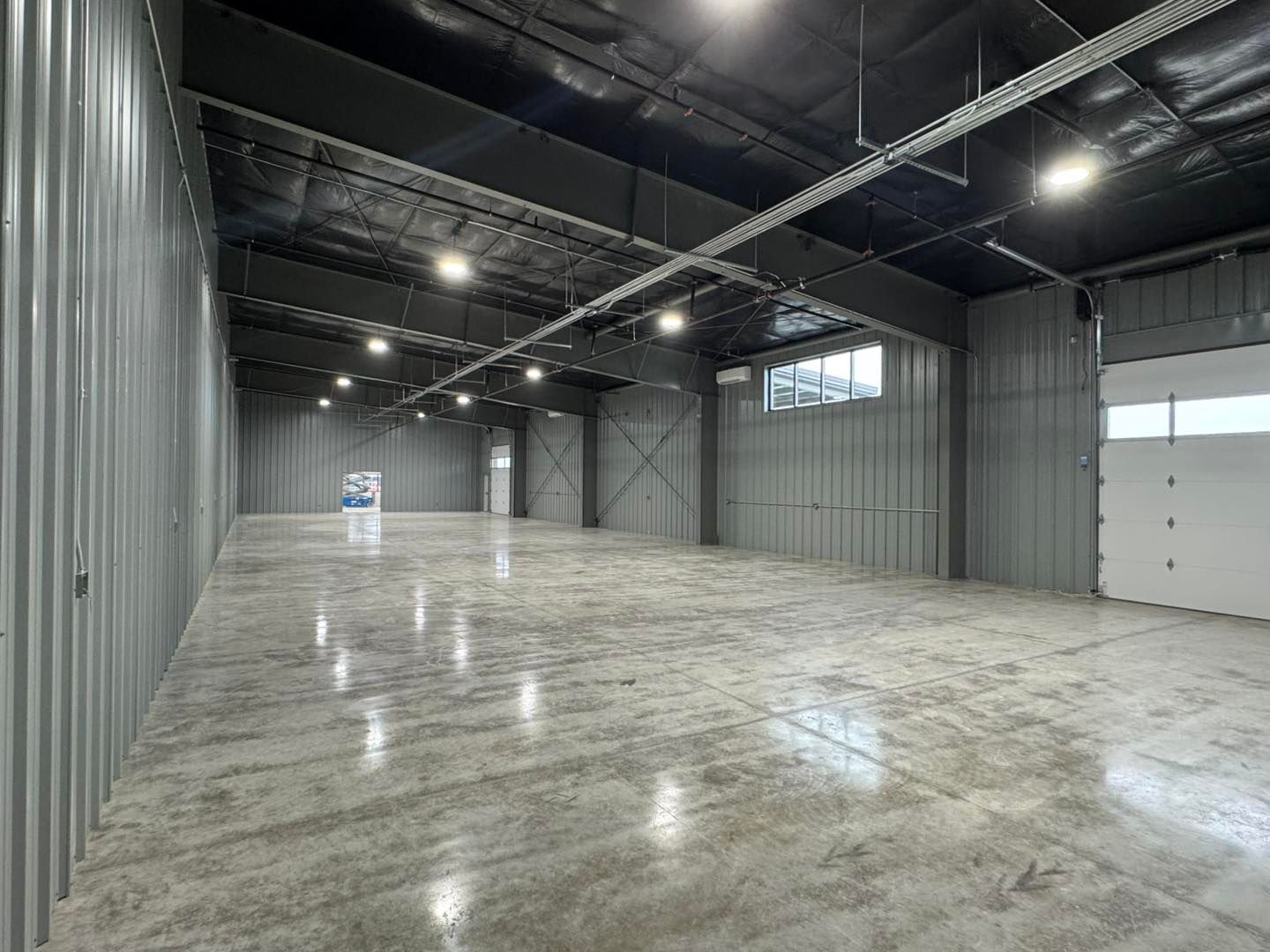 Empty industrial warehouse with gray metal walls, polished concrete floor, and overhead lights
