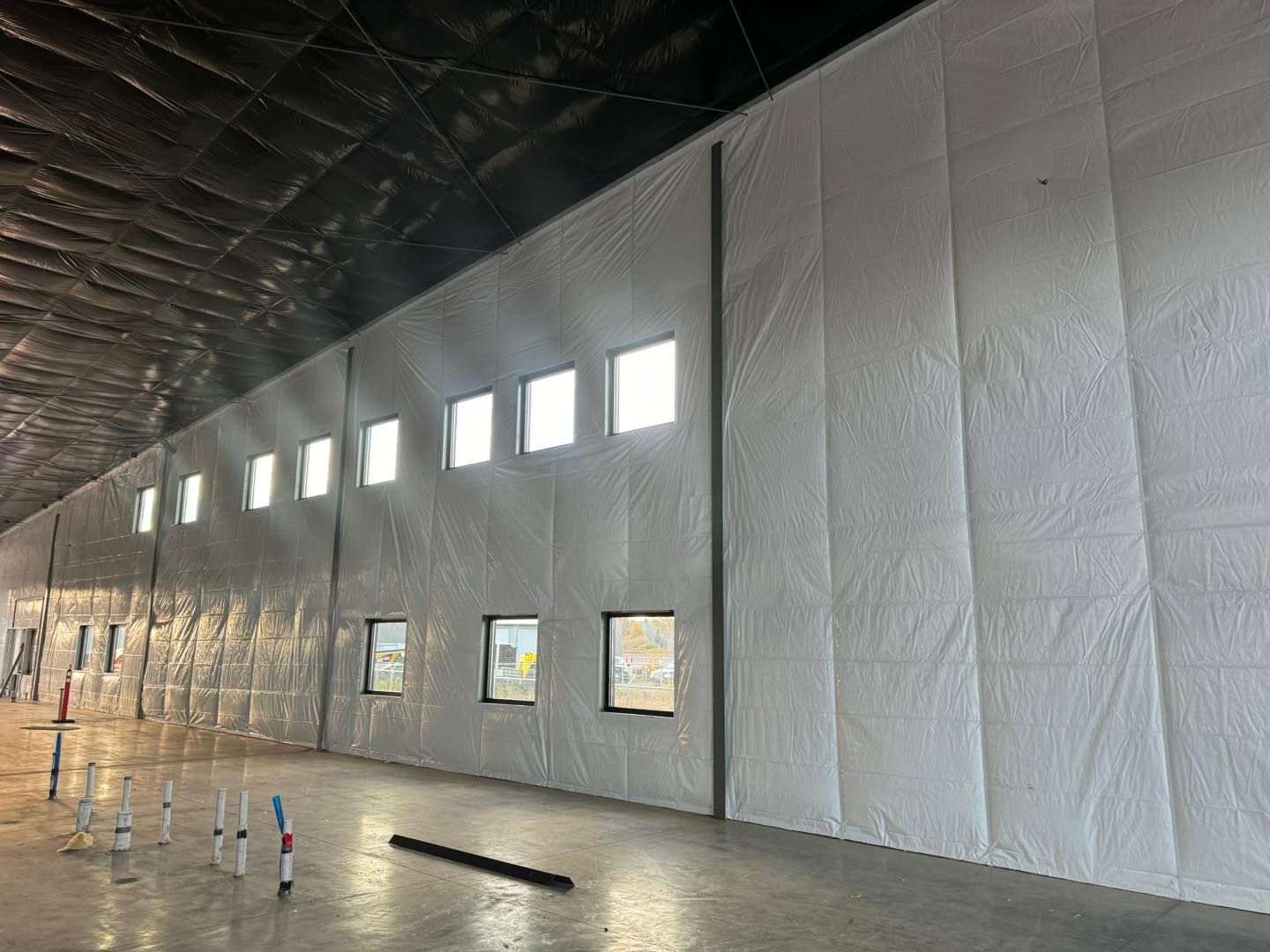 Interior of a large unfinished warehouse with insulated white walls, high windows, and concrete floor materials.