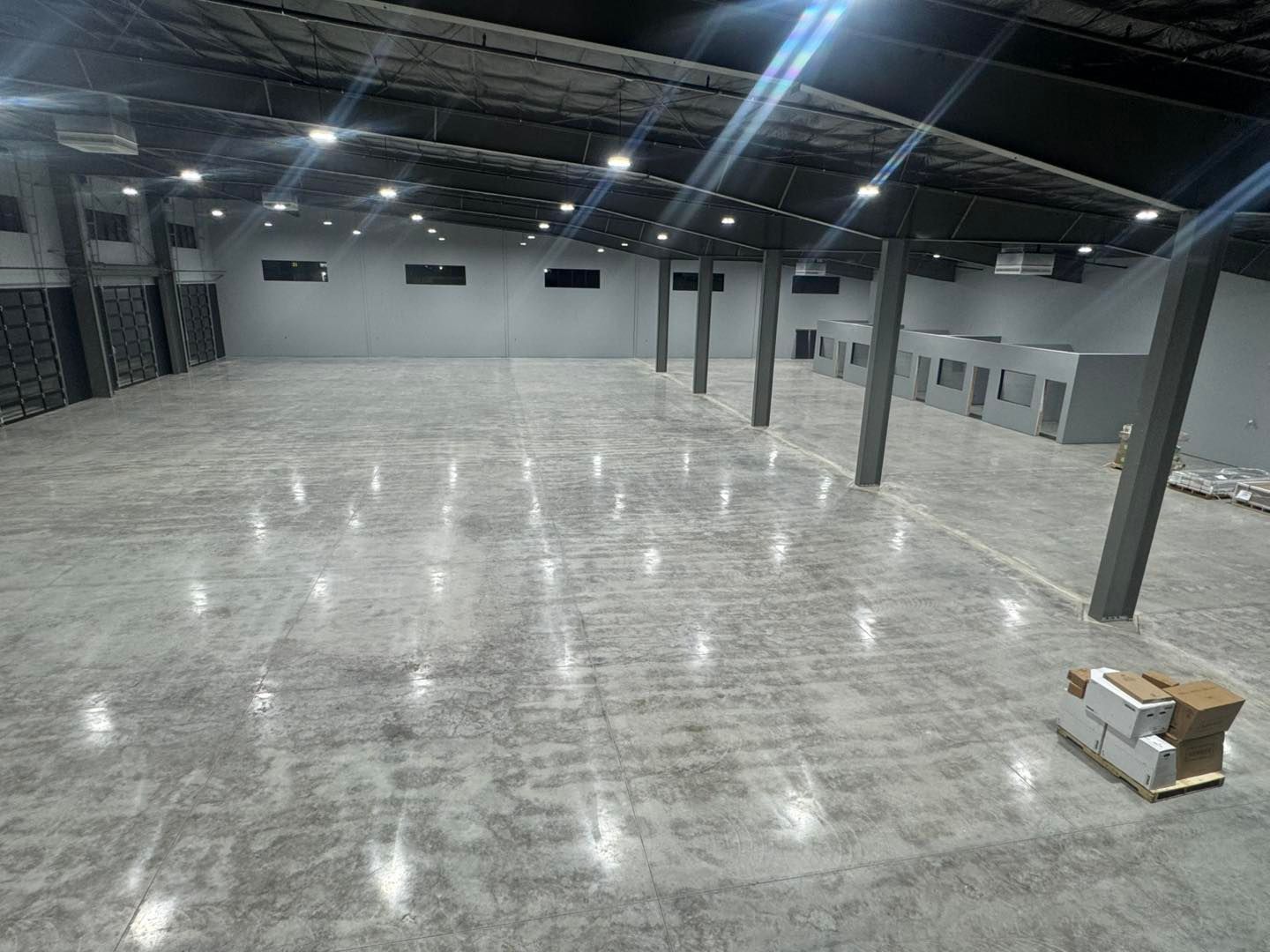 Empty industrial warehouse with polished concrete floor, columns, overhead lights, and a small box on the right