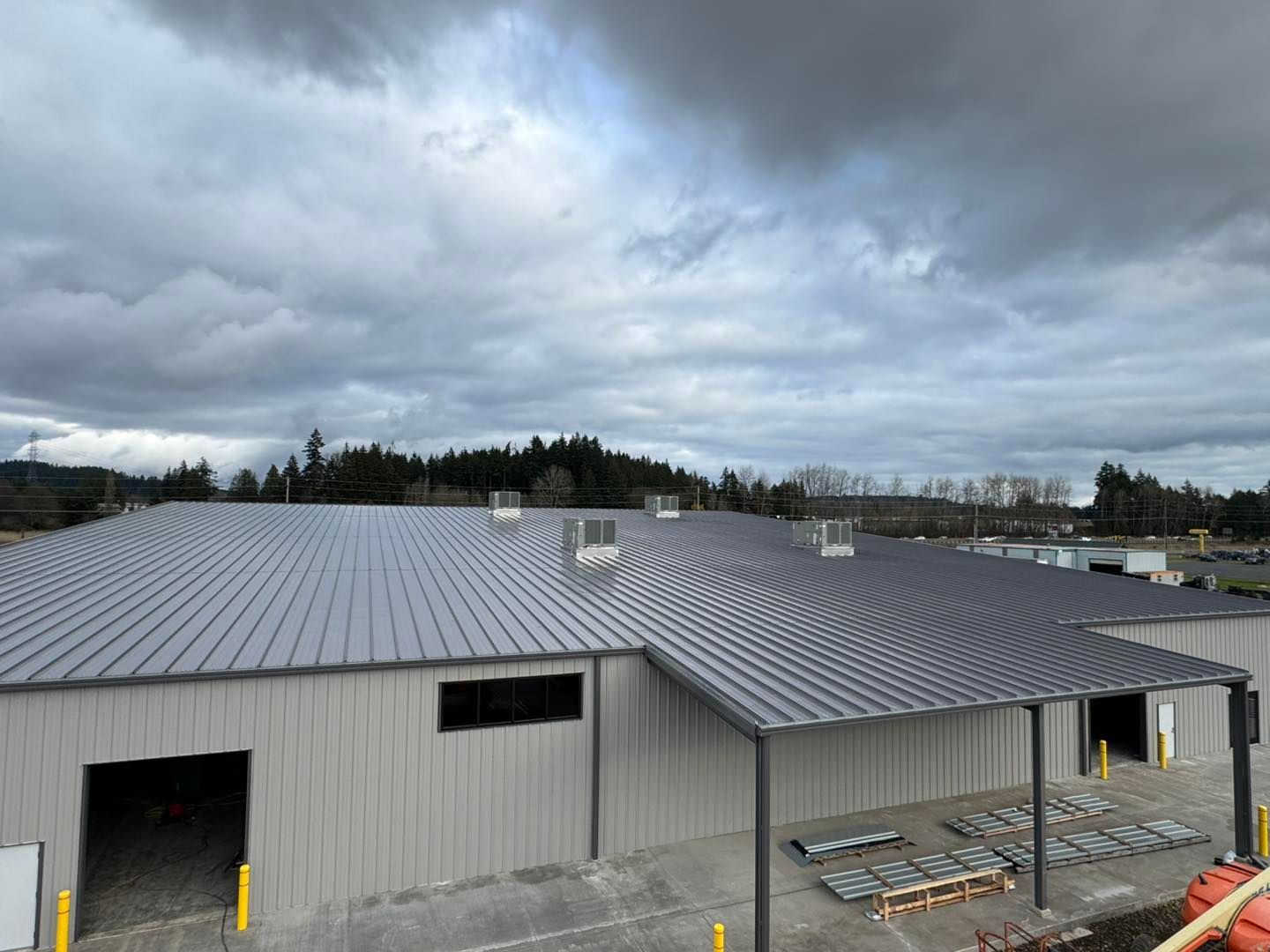 Large gray metal warehouse with a ribbed roof under cloudy skies, viewed from above