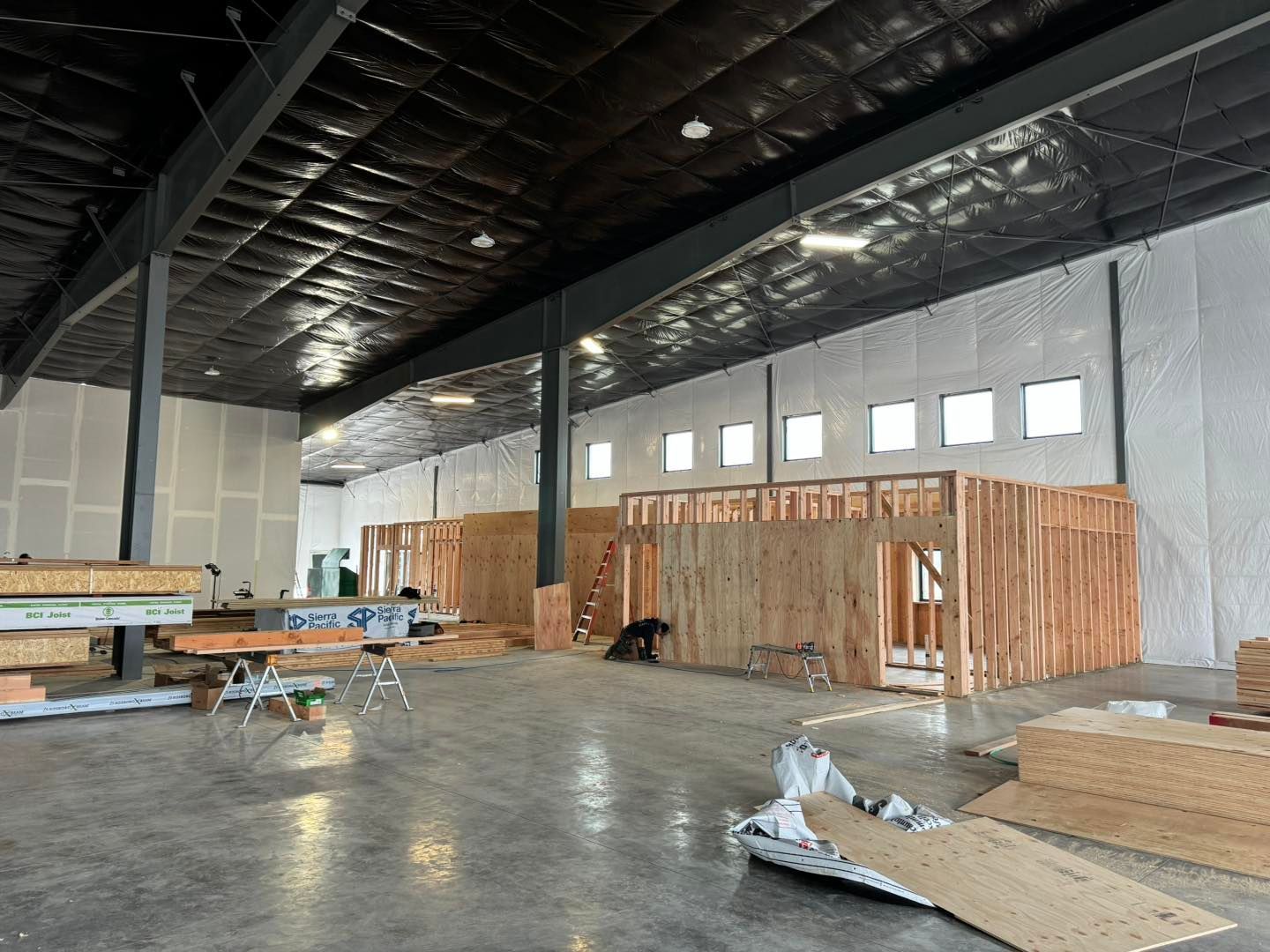 Empty warehouse interior with unfinished wood framing, exposed ceiling, and construction materials scattered on the floor