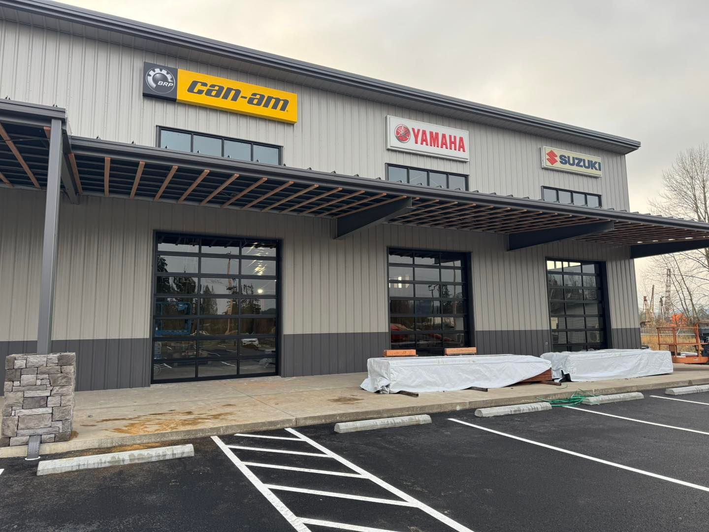 Exterior of a strip mall with storefront signs, large glass windows, and empty parking spaces under construction.