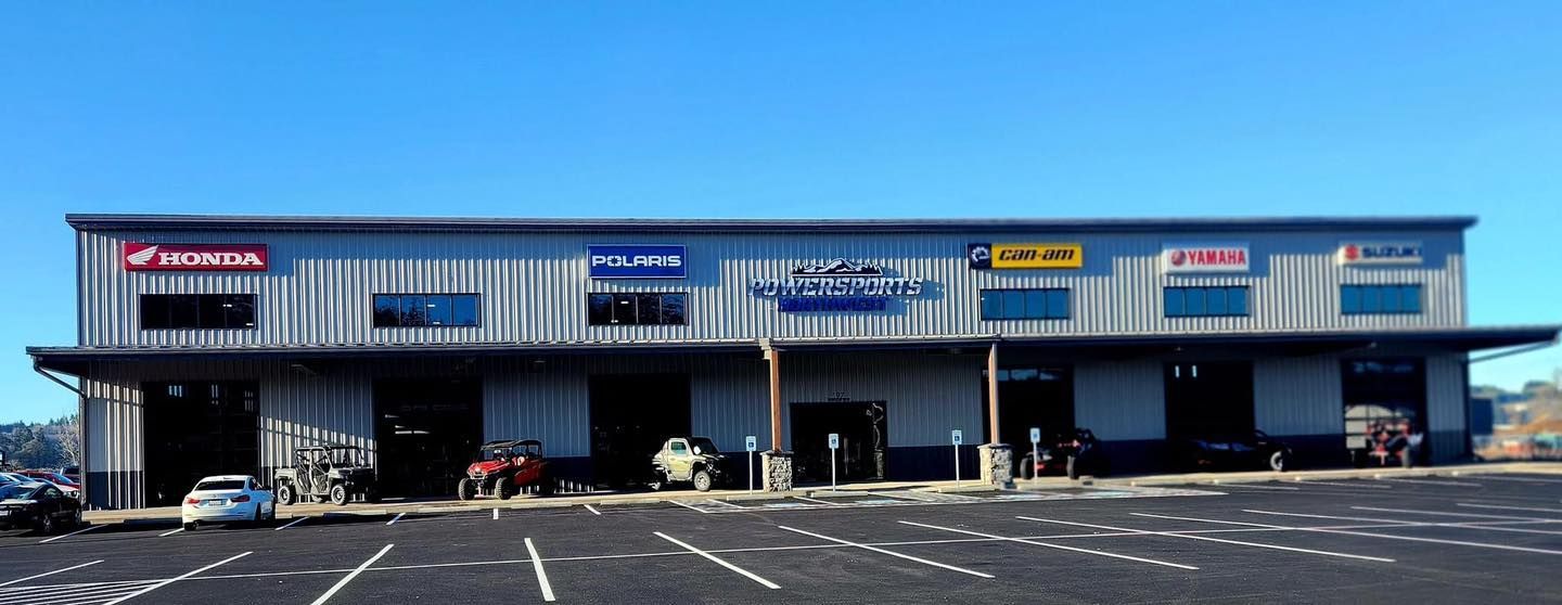 Blue strip mall storefronts with signs above empty parking spaces on a sunny day