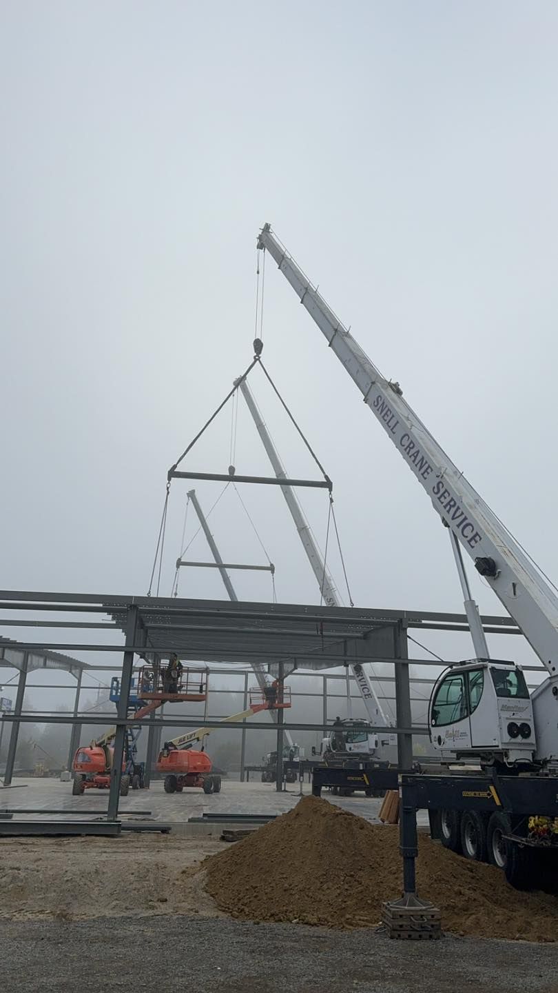 Construction site with steel frame being lifted by a crane in a gray, overcast setting.