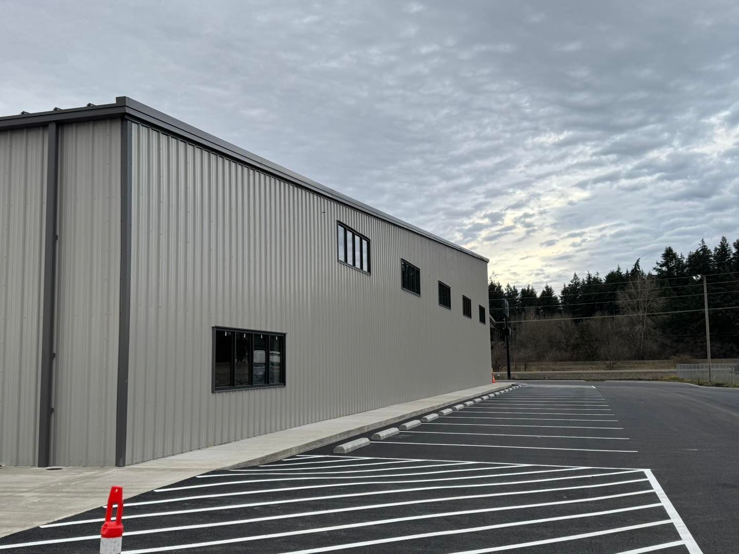 Gray warehouse beside empty striped parking lot under cloudy sky