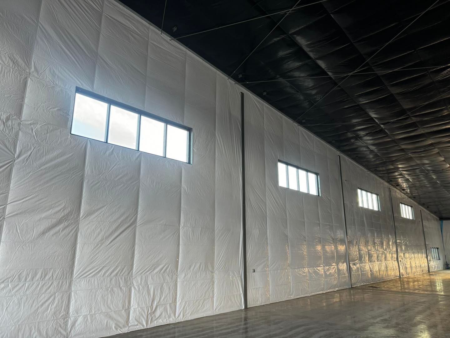 Insulated warehouse interior with white walls, small windows, and dark ceiling rafters