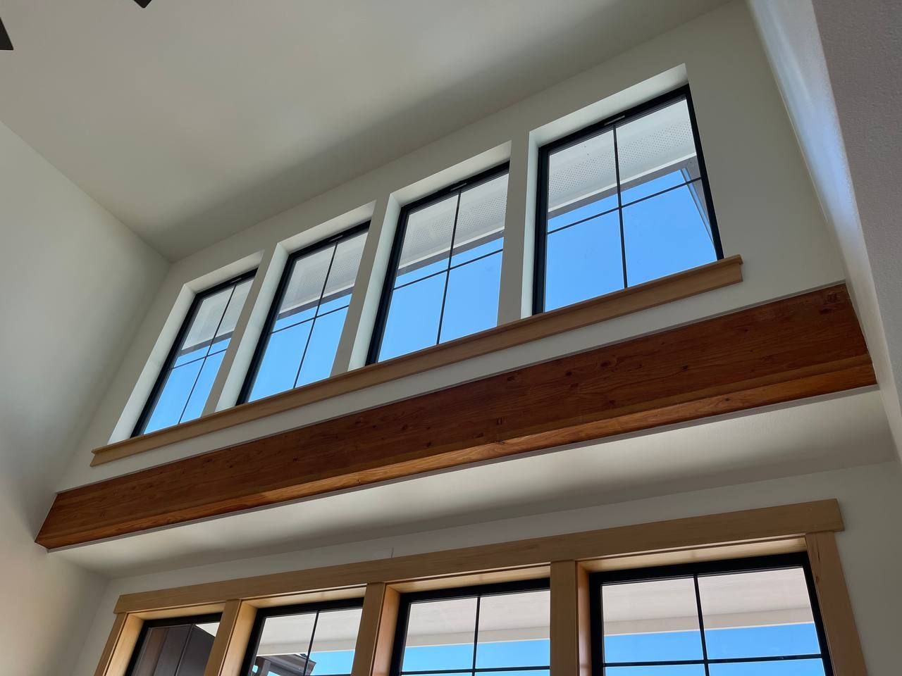 Tilted view of large indoor windows with white frames and a wooden beam beneath the ceiling.