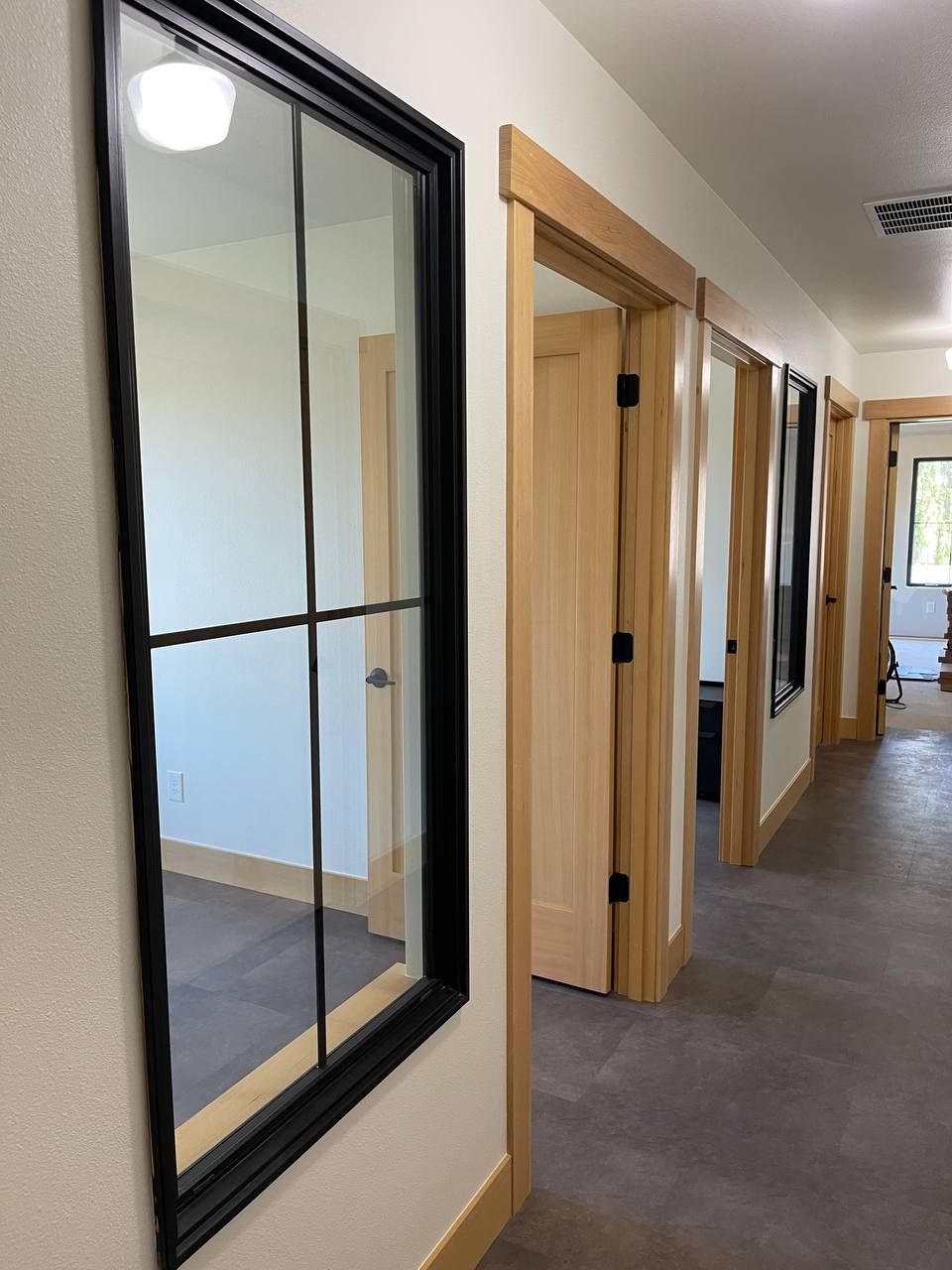 Bright hallway with wood-framed doorways and a black-framed glass panel on the left.