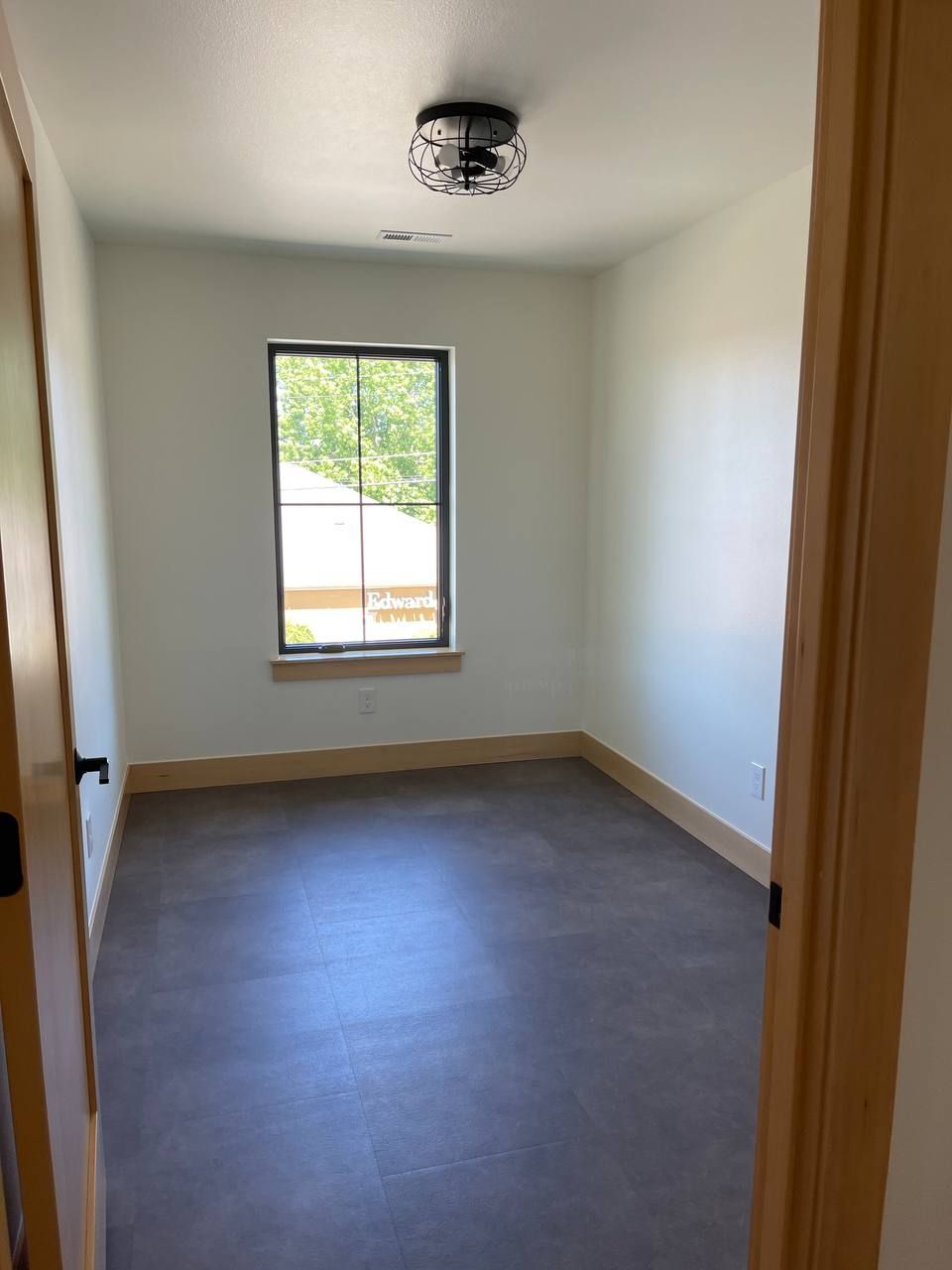 Empty small room with white walls, gray floor, and a single window.