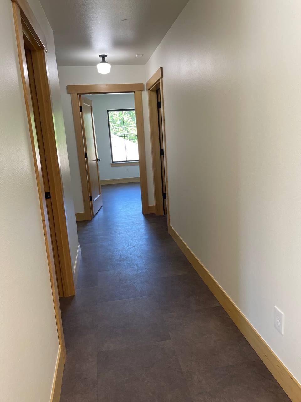 Narrow hallway with beige walls, wood trim, gray floor, and a window at the end.