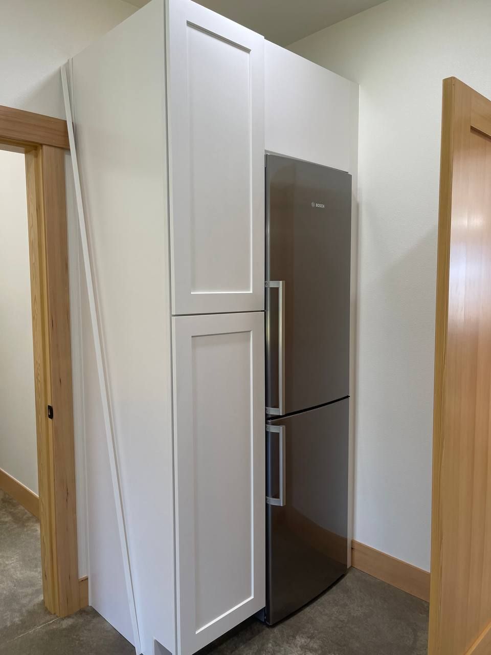 White built-in cabinet surrounding a stainless steel refrigerator in a kitchen hallway.