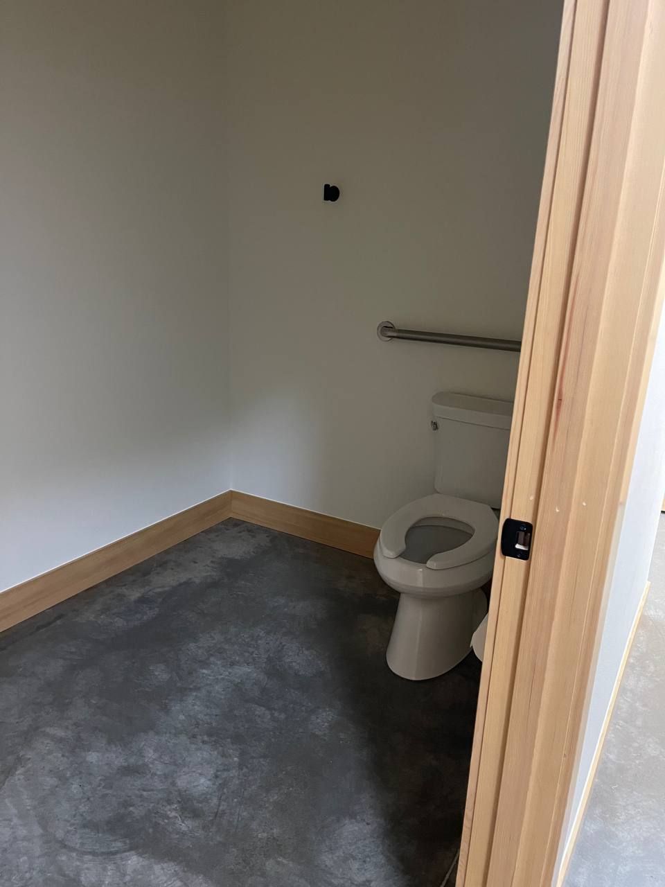 Small empty bathroom with toilet, gray floor, white walls, and a metal grab bar.