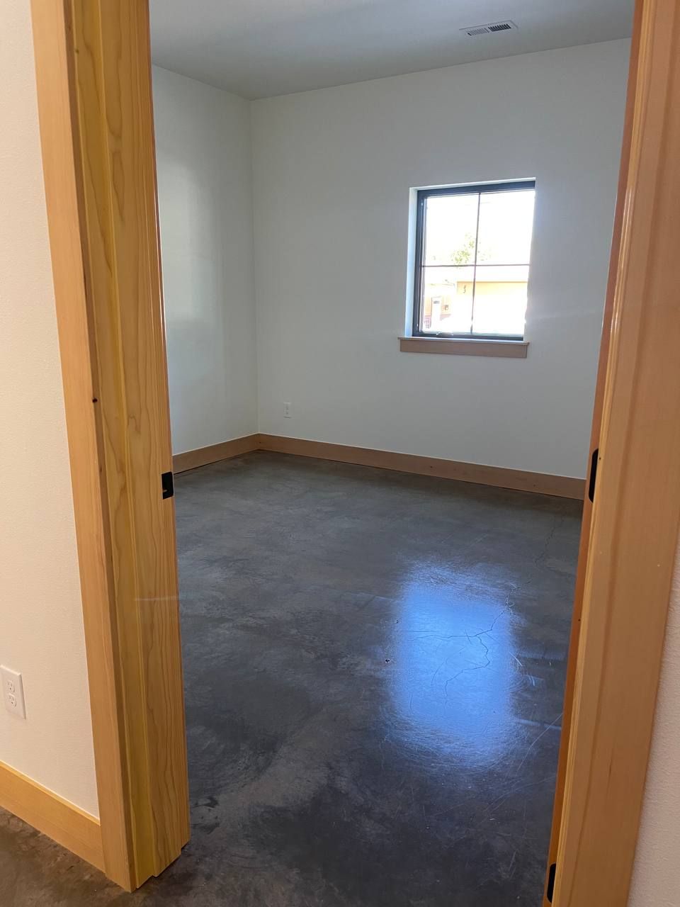 Empty room with gray floor, white walls, wood trim, and a small window.