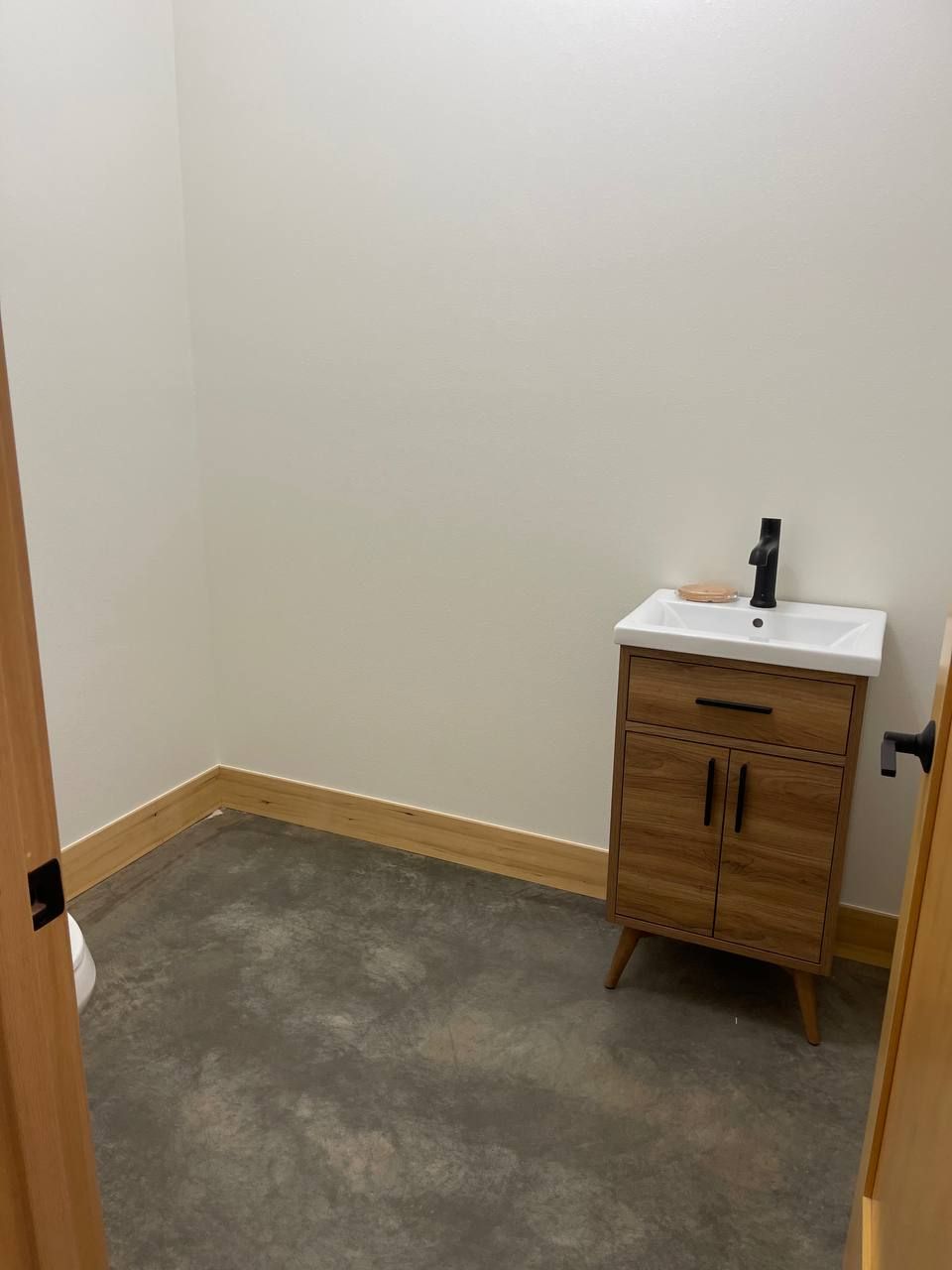 Small empty room with gray carpet, beige walls, and a wooden sink cabinet under a mirror.