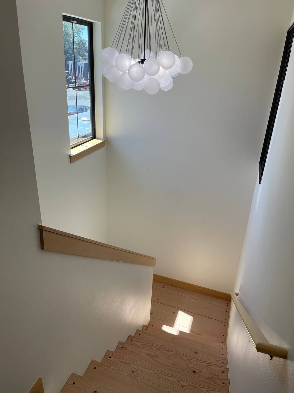 Stairwell with wooden steps, white walls, a hanging light fixture, and a window