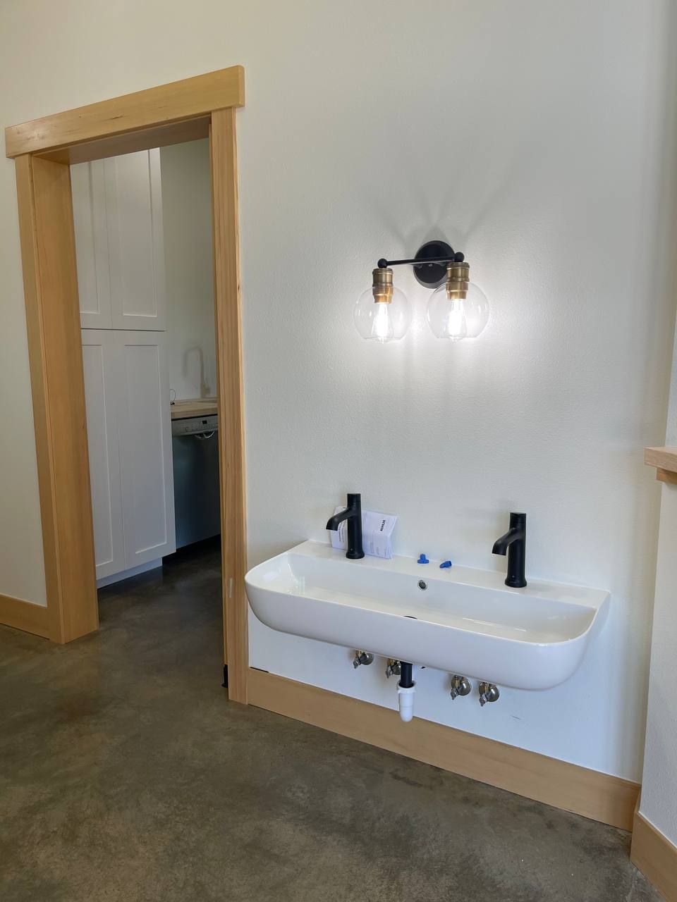 Modern bathroom with a wall-mounted sink, black faucets, mirror, and open doorway with wood trim