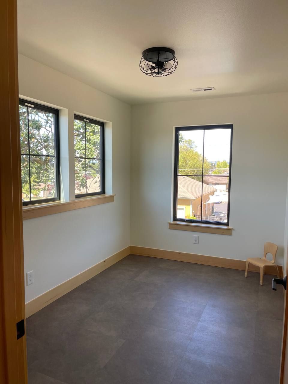 Empty room with gray floor, white walls, two windows, and a ceiling light fixture.