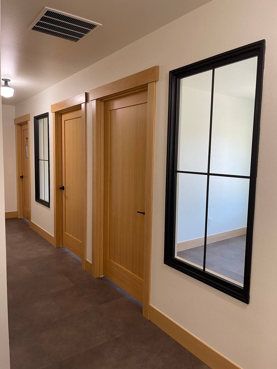 Hallway with wooden doors, beige walls, brown carpet, and black-framed windows.