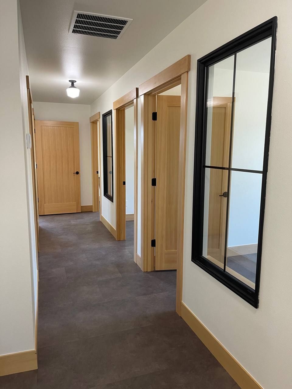 Empty office hallway with wood doors, white walls, and a dark carpeted floor