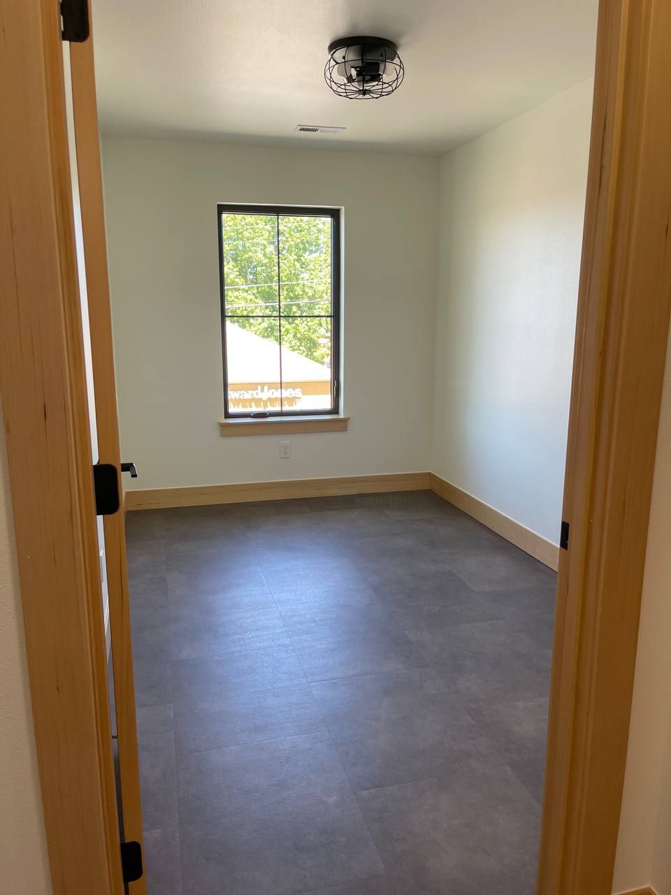 Empty small room with gray floor, white walls, wood trim, and a window looking outside.