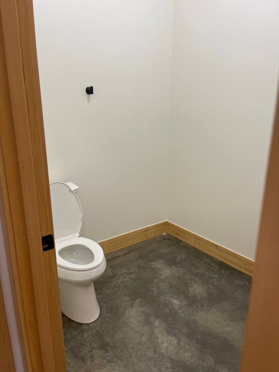 Small empty bathroom with toilet and gray floor, viewed through an open doorway.