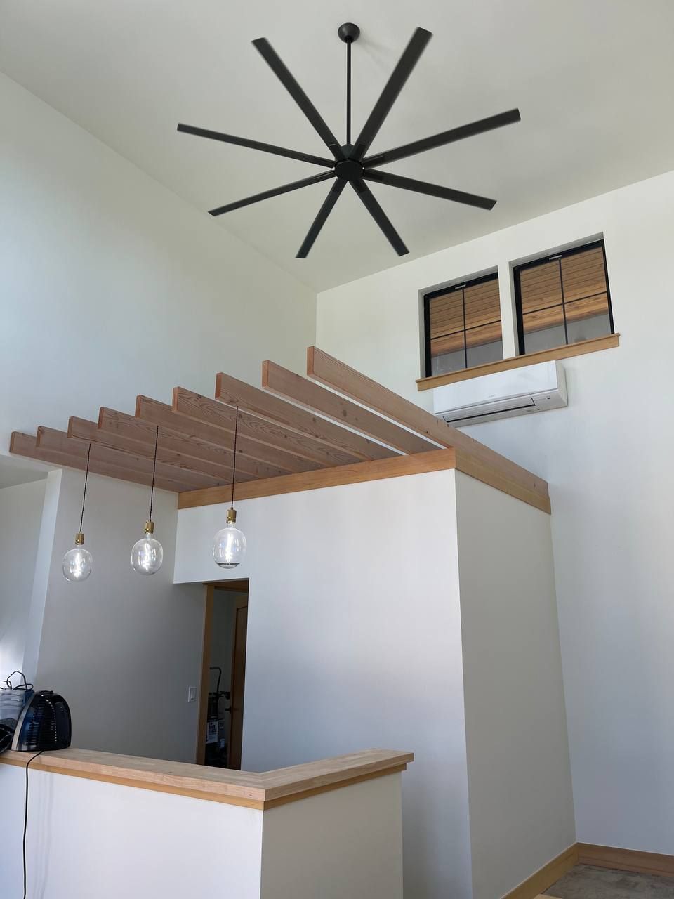 Modern interior with high ceiling, black starburst light fixture, wooden beam pergola, and hanging pendant lights