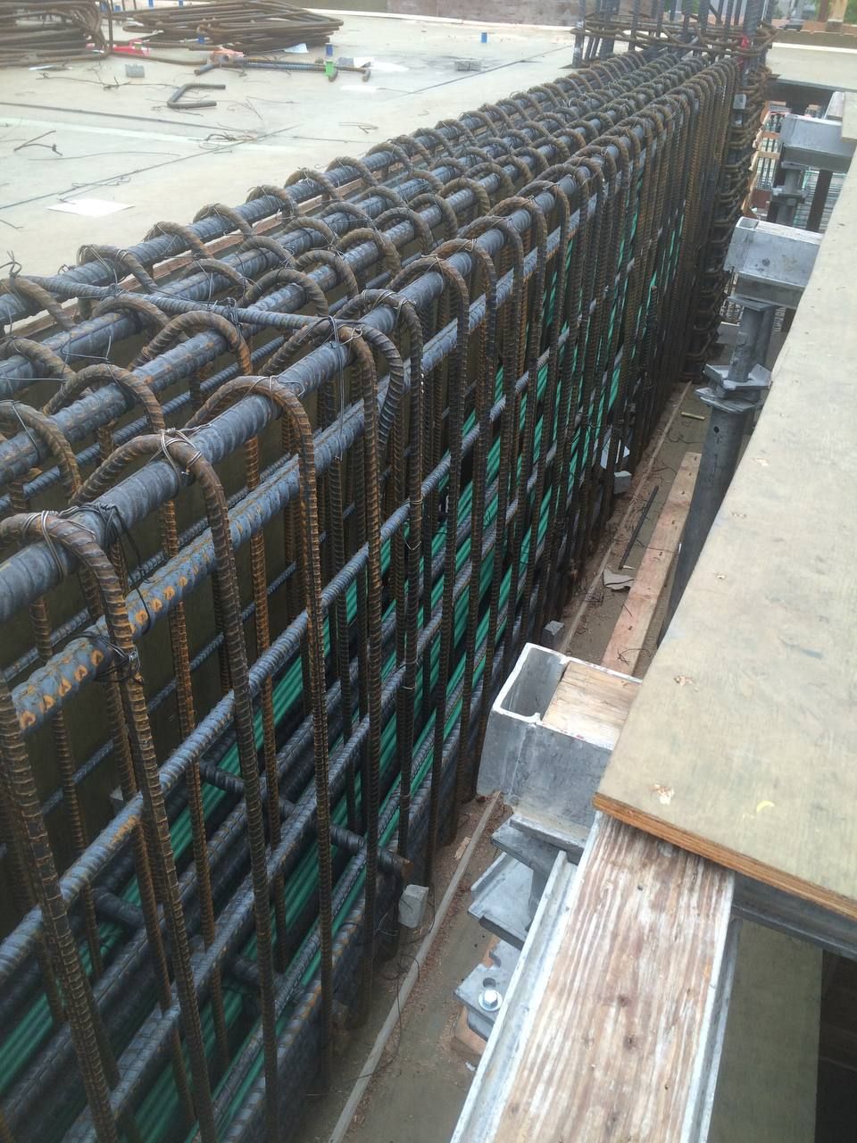 Long rebar cage for concrete foundation, with green formwork at a construction site