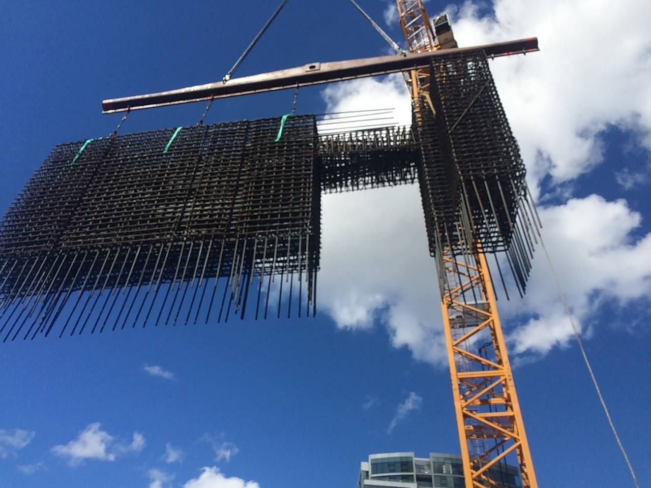 Construction crane lifting rebar framework against a blue sky with clouds