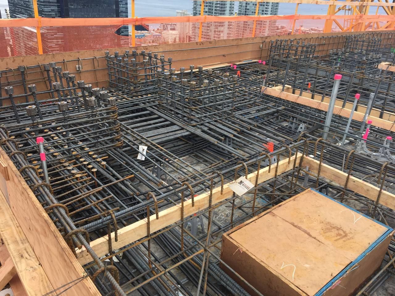 Rebar framework at a construction site, with wooden formwork and orange safety fencing.
