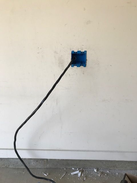 A black cord is plugged into a blue box on a white wall.