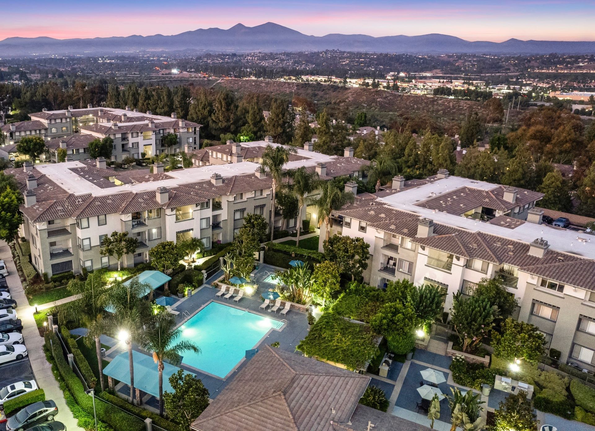 Aerial view of a multi-building apartment complex with a central pool and lush landscaping at dusk at Alize Apartment Homes in Aliso Viejo, CA.