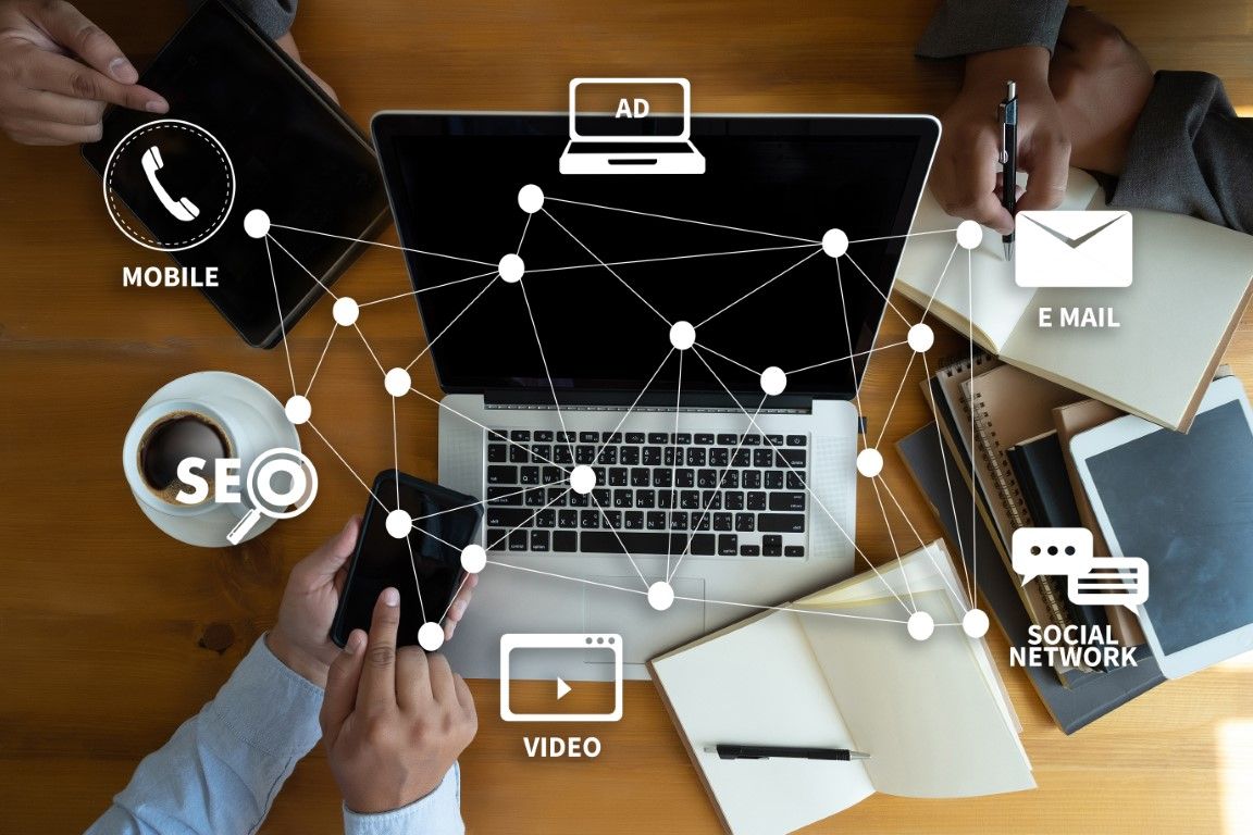 Overhead view of people collaborating with a laptop, phones, and notebooks; digital marketing icons overlay.