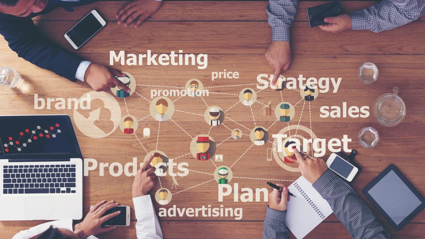Business team planning around a wooden table with marketing terms and connected icons.